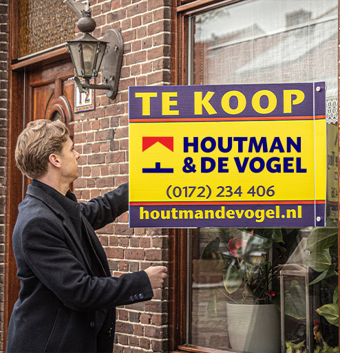 makelaar hangt bord aan raam van woning